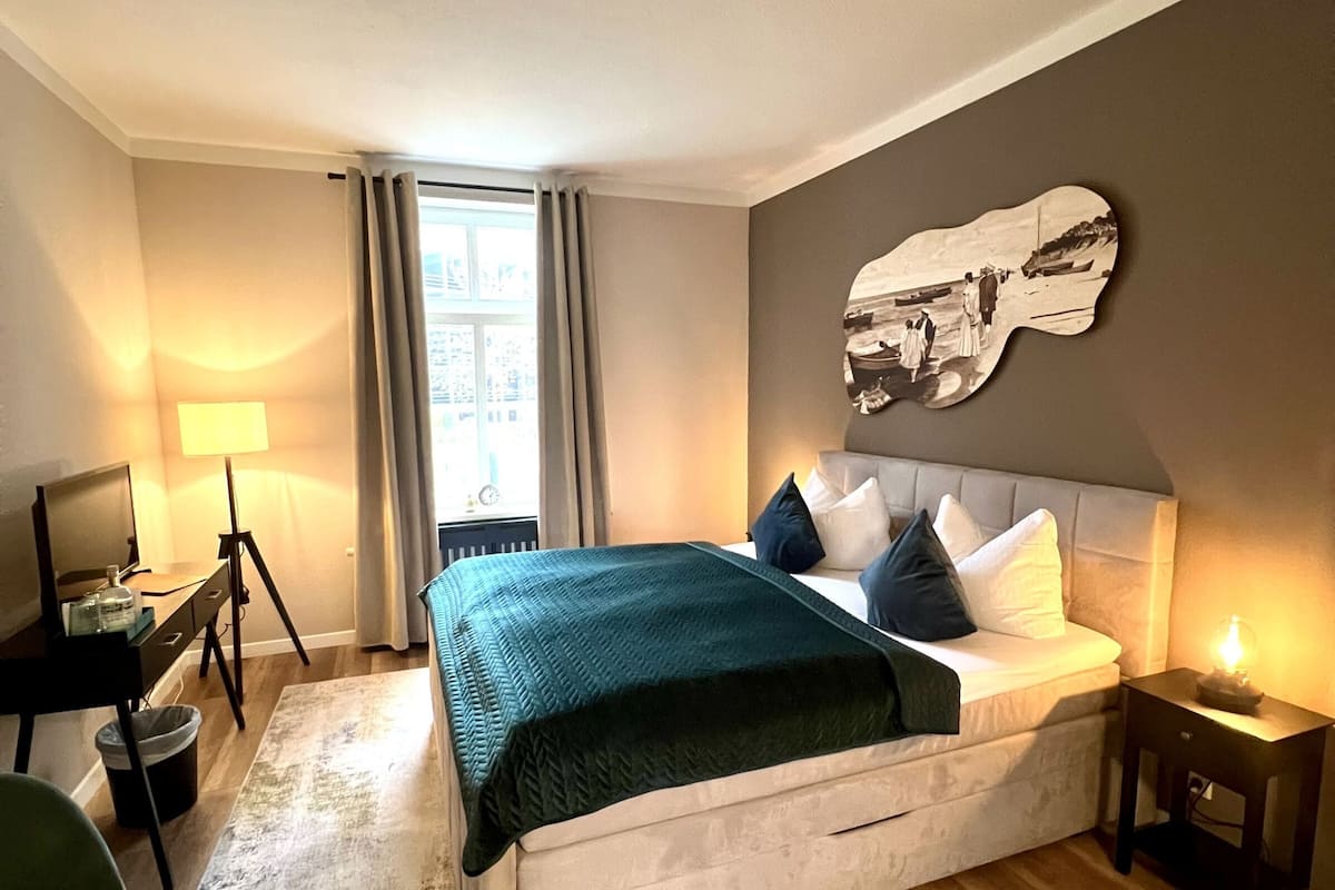 A modern hotel room with a large bed, a desk, a chair, and a view of the city.
