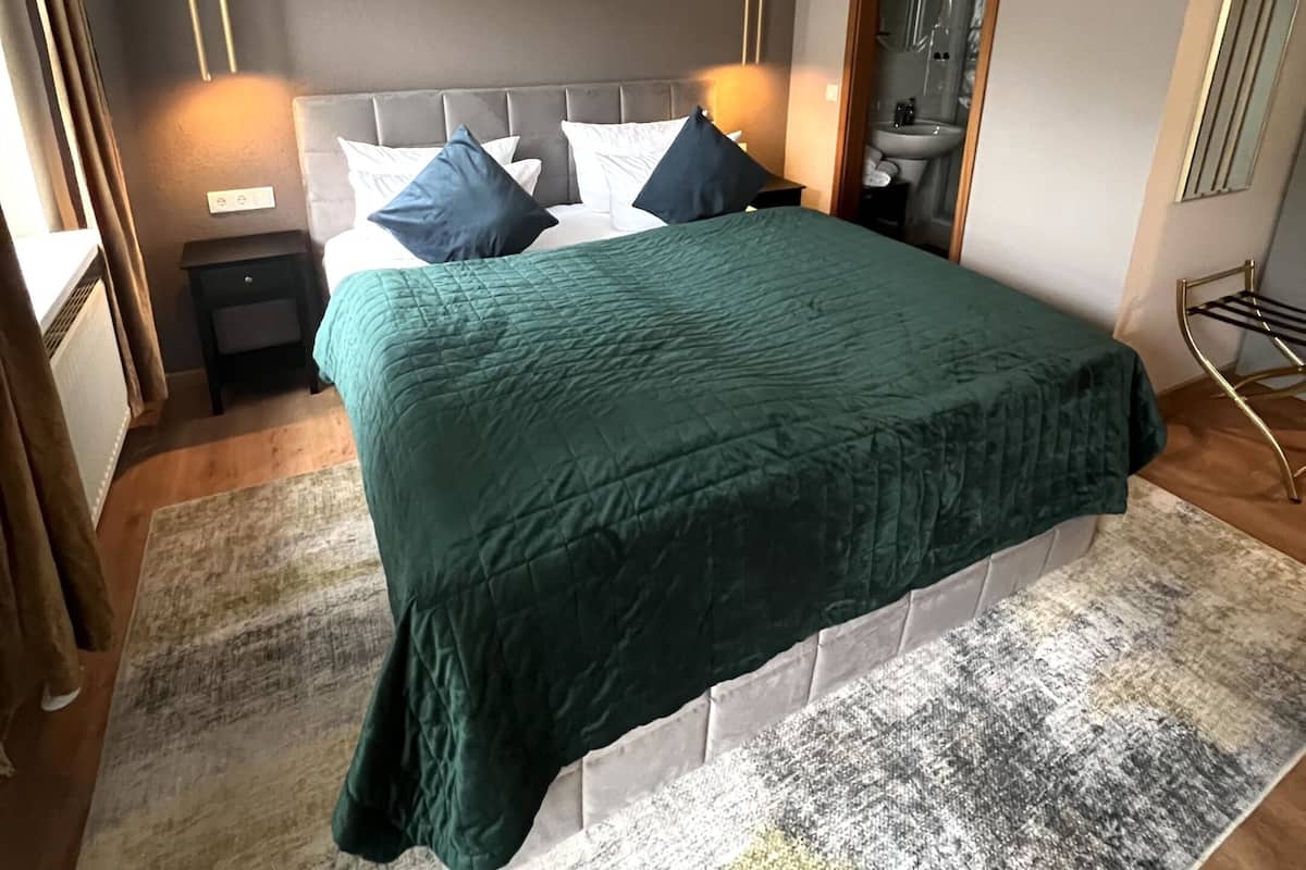 A bedroom with a large bed, two bedside tables, a nightstand, a mirror, and a window with curtains.