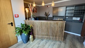 A reception area with a wooden counter, potted plants, and hanging pendant lights. - Hotel Balticpetite (Heringsdorf)