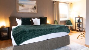 A neatly arranged bedroom with a bed, bedside table, lamp, and a painting of a beach scene. - Hotel Balticpetite (Heringsdorf)