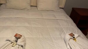 A neatly made bed with white bedding and towels folded at the foot of the bed. - West Palm Hotel (Chaguaramas)