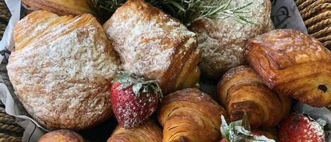Variedad de pasteles, incluyendo cruasanes y scones, algunos con fresas, dispuestos en una bandeja.