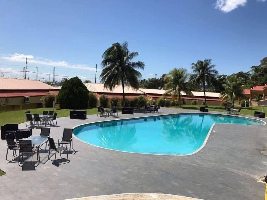 A swimming pool with lounge chairs and tables, surrounded by palm trees and buildings with red roofs.