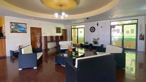 A spacious lobby with a curved ceiling, a reception desk, seating areas, and large windows offering a view of the outdoors. - West Palm Hotel (Chaguaramas)