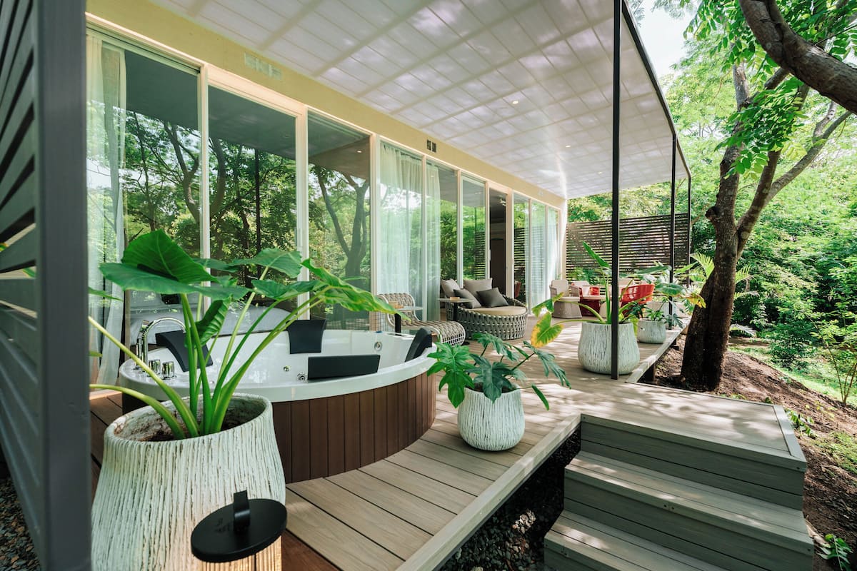 A modern outdoor lounge area with a wooden deck, seating, and potted plants.
