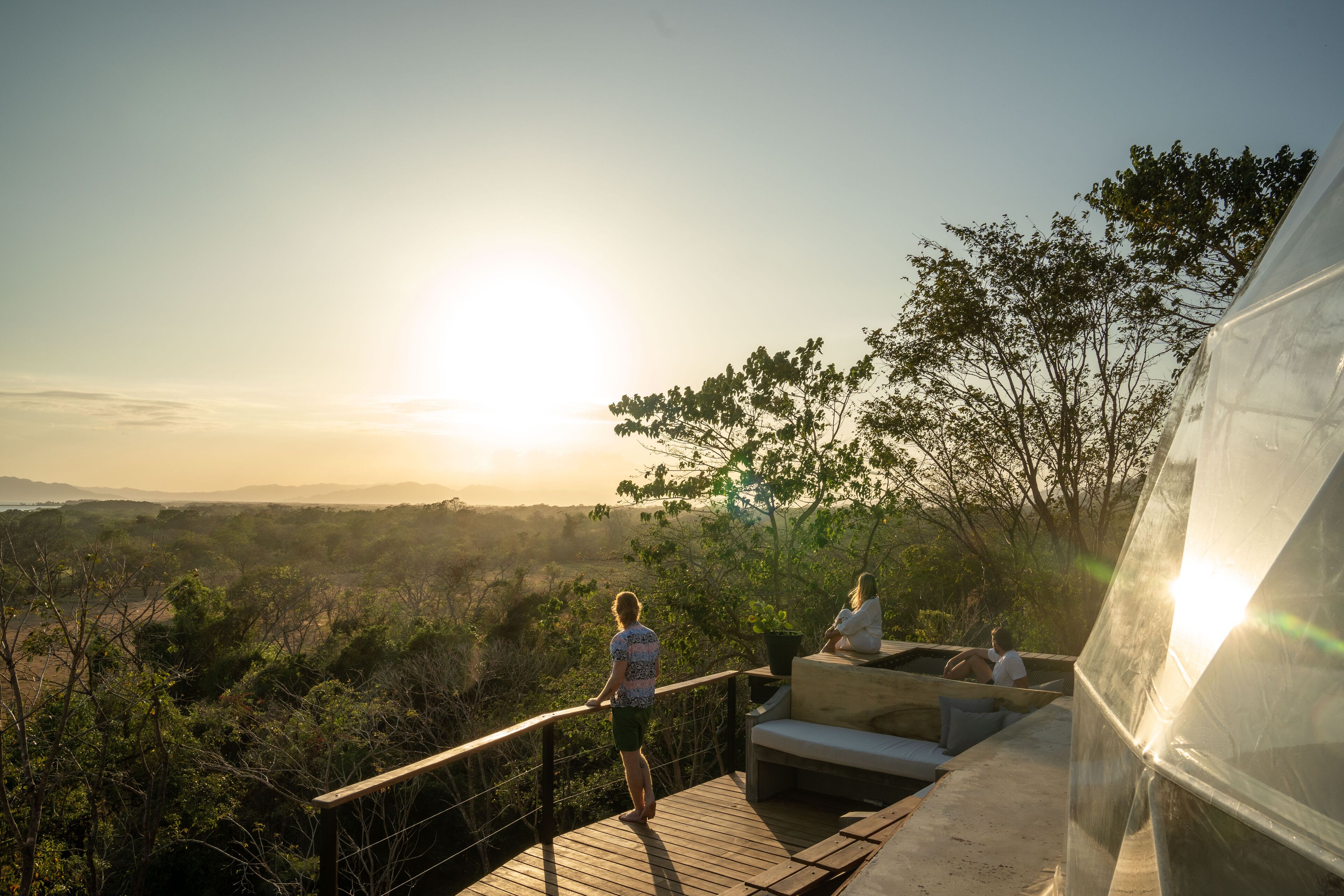 A wooden deck with a railing overlooking a landscape with trees and a distant view of mountains.