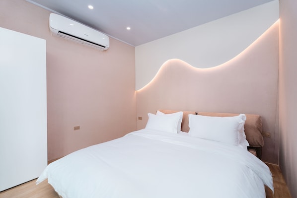 Un dormitorio moderno con una cama, ropa de cama blanca, un aire acondicionado de pared y un original diseño de luz ondulada en la pared.