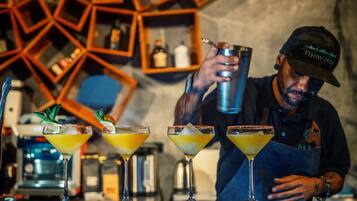 Un barman preparando cócteles en una barra, con una estantería geométrica moderna al fondo.