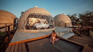 Un edificio moderno de forma abovedada con fachada de vidrio, terraza de madera y zona de piscina.