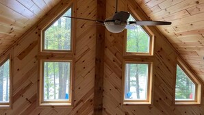 A room with a sloped ceiling, wooden walls, and four windows.