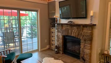 A cozy living room with a stone fireplace, a television mounted above it, and a sliding glass door leading to an outdoor patio.