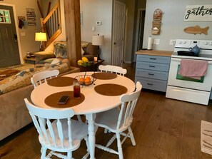 A dining area with a round table, white chairs, and a bowl of fruit.