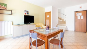 A dining area with a table, chairs, a television, and a staircase in the background. - Beachside Villa in Paestum (Capaccio-Paestum)