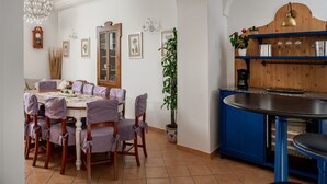 A dining area with a wooden table and chairs, a chandelier, and a cabinet with shelves.