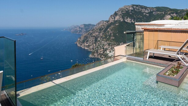 A rooftop infinity pool with a clear view of the sea and mountains.