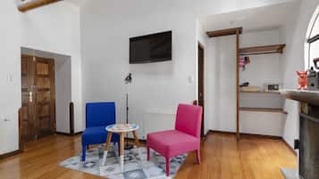 Sala de estar com piso de madeira, TV na parede, lareira e uma poltrona azul e rosa.