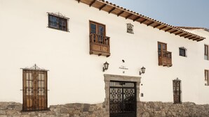 A building with a stone base, multiple wooden balconies, and a black gate. - Andenes (Cusco)