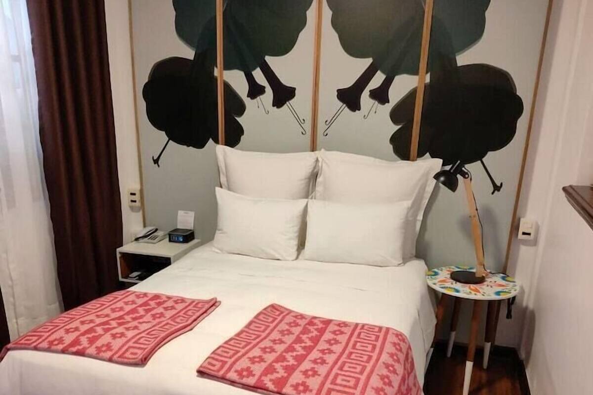 Una habitación de hotel con una cama, una mesita de noche y una lámpara de pared.