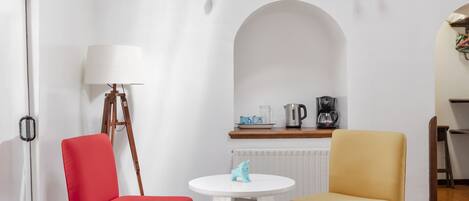 Una habitación con piso de madera, una silla roja, una silla amarilla, una mesa blanca y una lámpara.