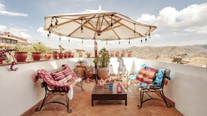 A terrace with two chairs, a table, and an umbrella. There are potted plants and a white horse statue. - Andenes (Cusco)