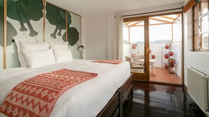 A hotel room with a large bed, a view of the outdoors, and a balcony with potted plants. - Andenes (Cusco)