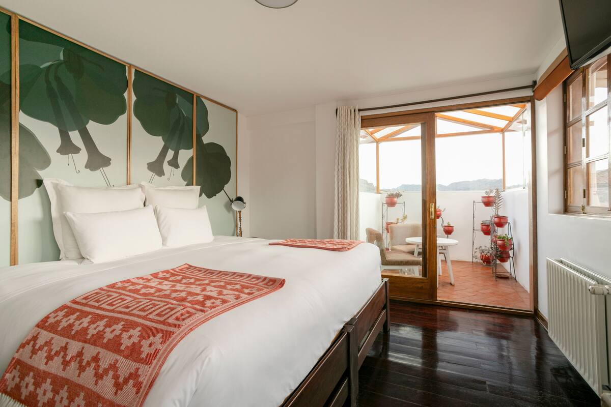 Habitación de hotel con una cama grande, vistas al exterior y un balcón con plantas en macetas.