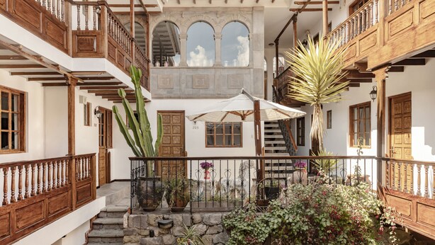 A courtyard with a stone staircase, wooden balconies, and potted plants. - Andenes (Cusco)