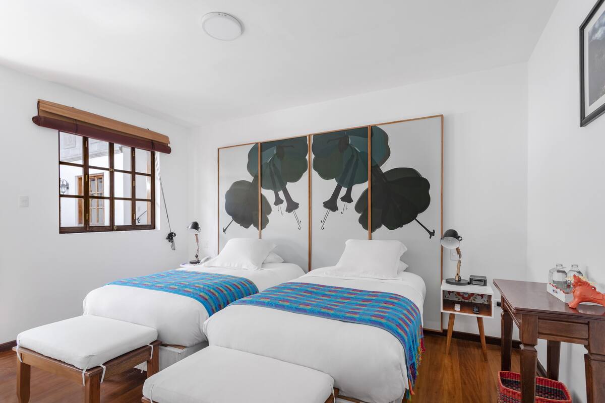 Una habitación con dos camas, una ventana, un cuadro, un escritorio y una silla.