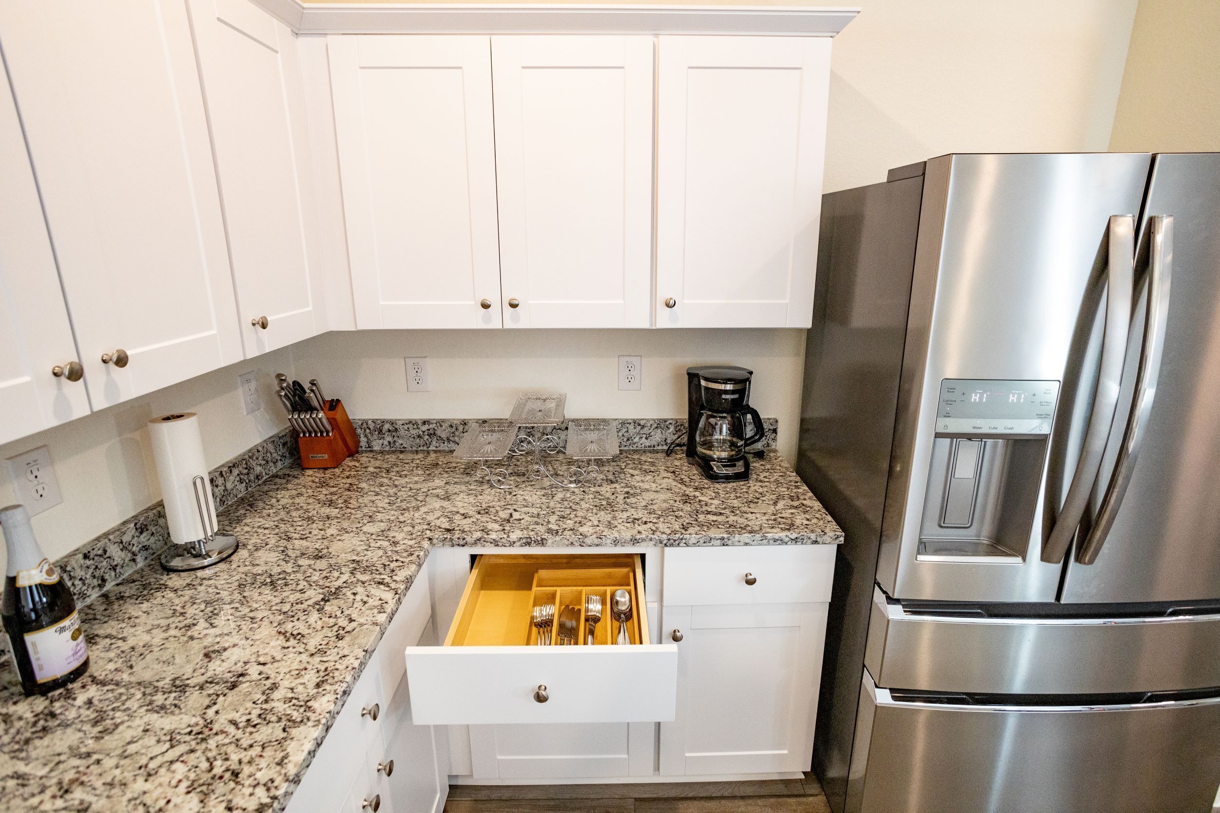 A kitchen with white cabinets, a stainless steel refrigerator, a drawer organizer, and a coffee maker.