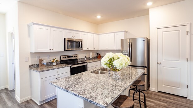 A modern kitchen with white cabinets, granite countertops, stainless steel appliances, and a central island with bar stools.