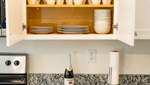 A kitchen with a marble countertop, a cabinet with dishes, and a bottle of champagne.