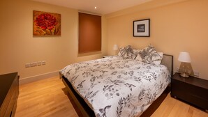 Une chambre à coucher avec un lit, une table de chevet, une lampe, un tableau et une fenêtre.