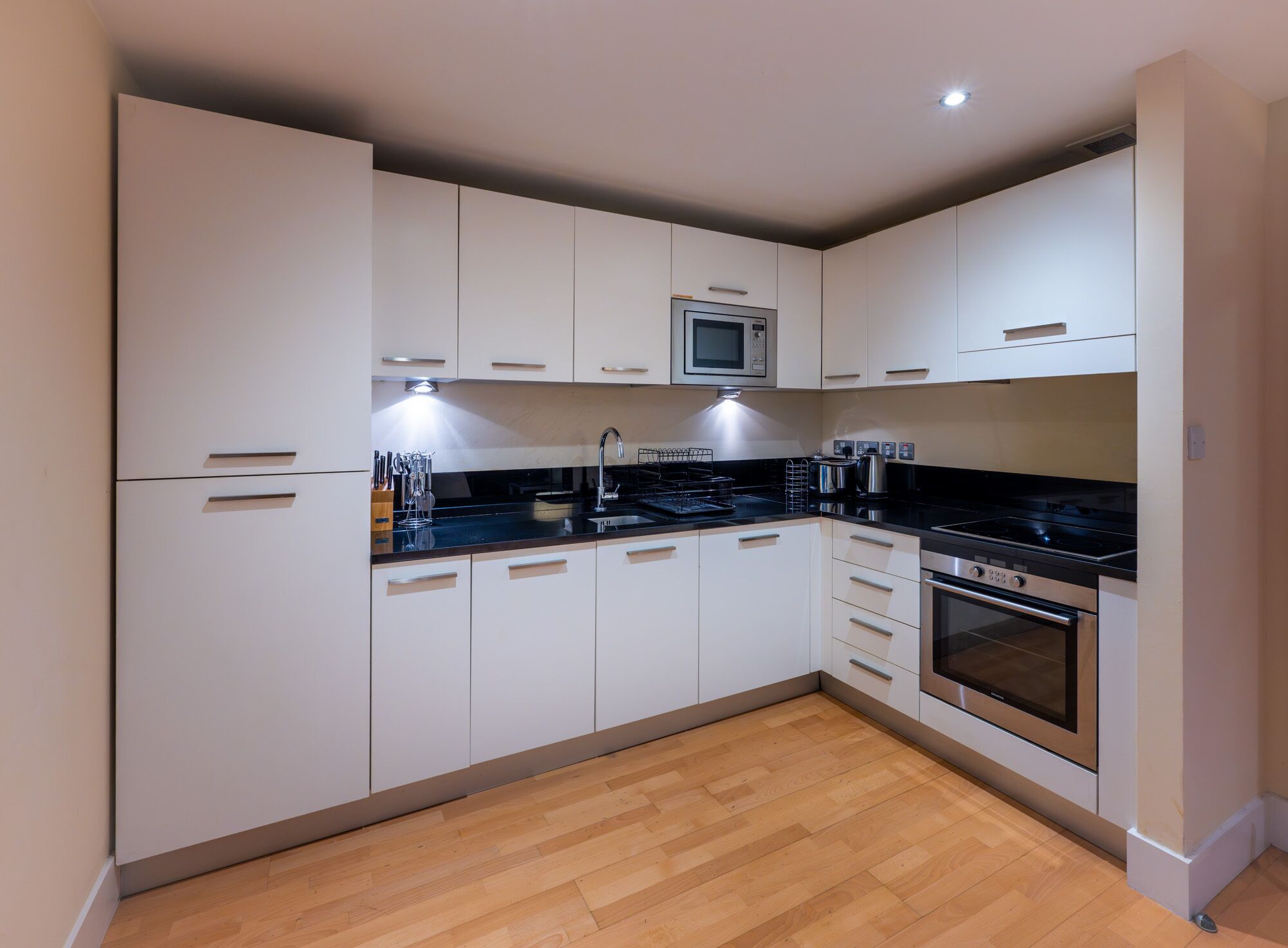 A modern kitchen with white cabinets, a black countertop, stainless steel appliances, and a wooden floor.