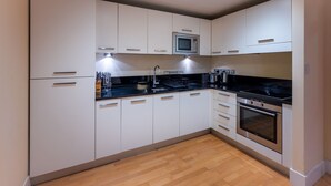 Une cuisine moderne avec des meubles blancs, un plan de travail noir, des appareils électroménagers en acier inoxydable et un plancher en bois.