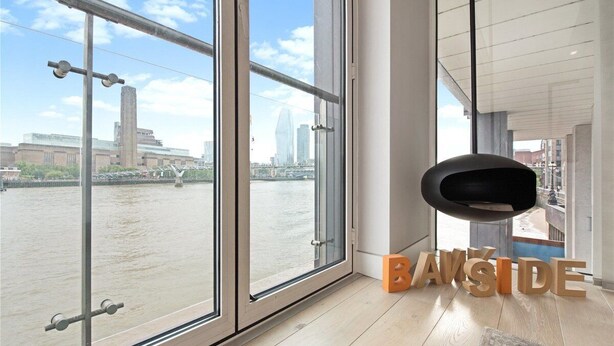 Une chambre moderne dotée de grandes fenêtres donnant sur une rivière et sur le paysage urbain.
