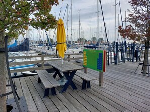 A wooden pier with picnic tables and a yellow umbrella, overlooking a marina with numerous boats. - Luxury Houseboat in Volendam Marina (Volendam)
