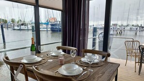 Een eettafel gedekt met borden, glazen en een fles, met uitzicht op een jachthaven met boten.