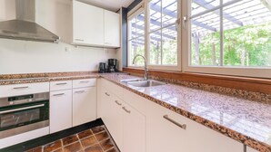 A kitchen with white cabinets, a stainless steel range hood, a built-in oven, granite countertops, a window with a view of greenery, and a sink. - Holiday Home in Gelderland Near Den Bramel (Lochem)