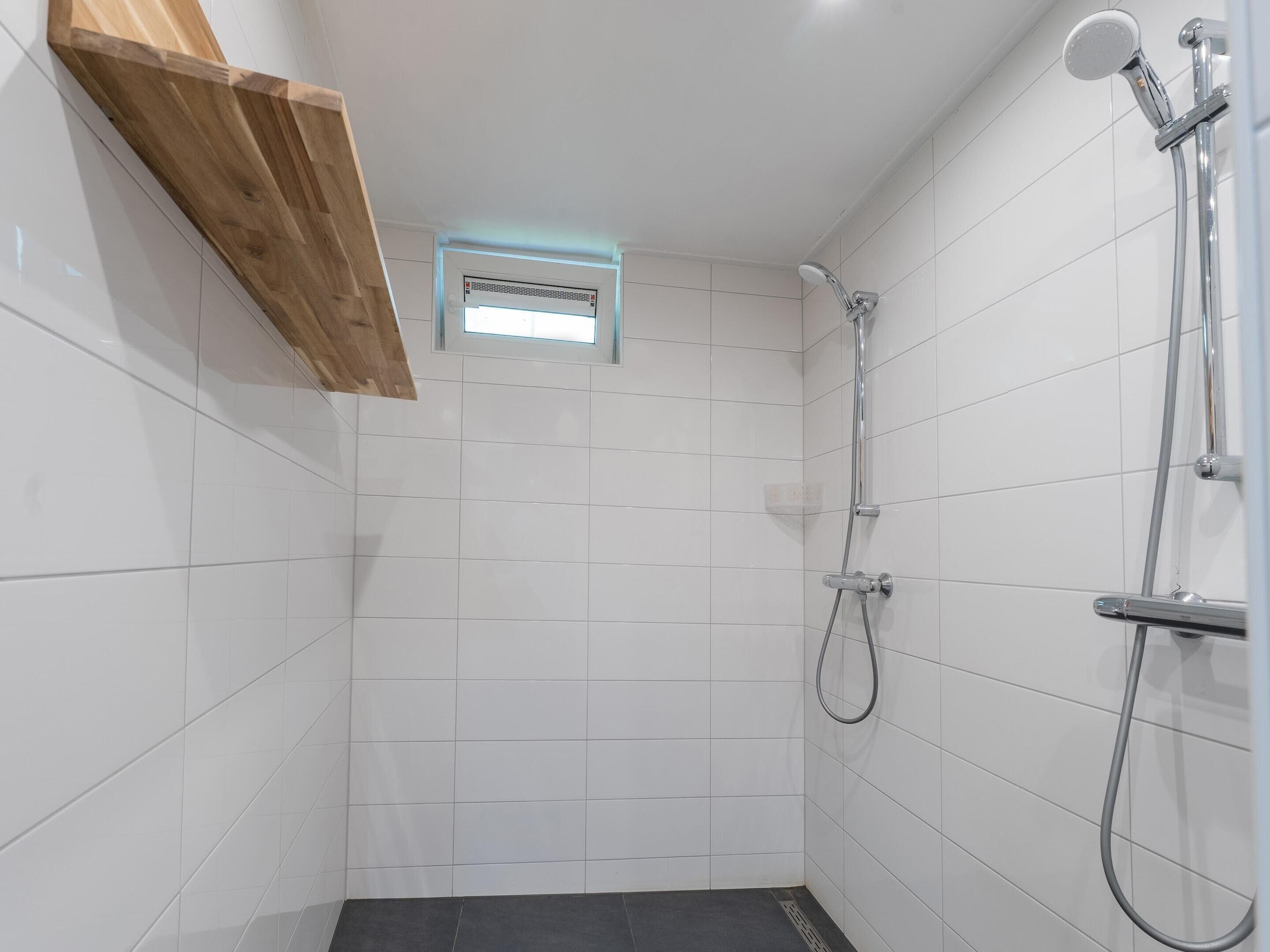 A small, tiled shower room with a wooden shelf and a ventilation vent.