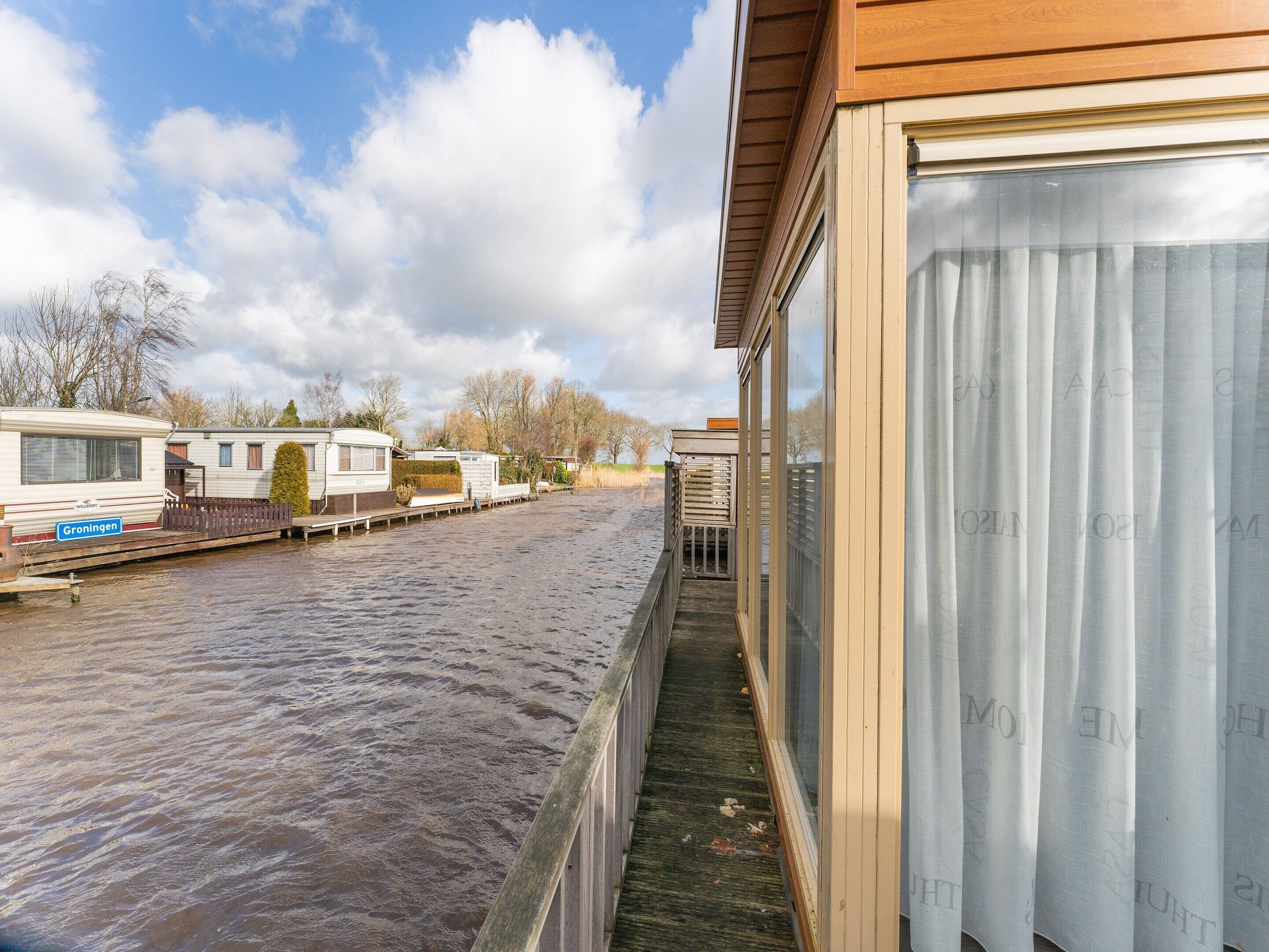 Une vue sur le canal, avec une rangée de maisons mobiles et un bâtiment en bois doté de grandes fenêtres.