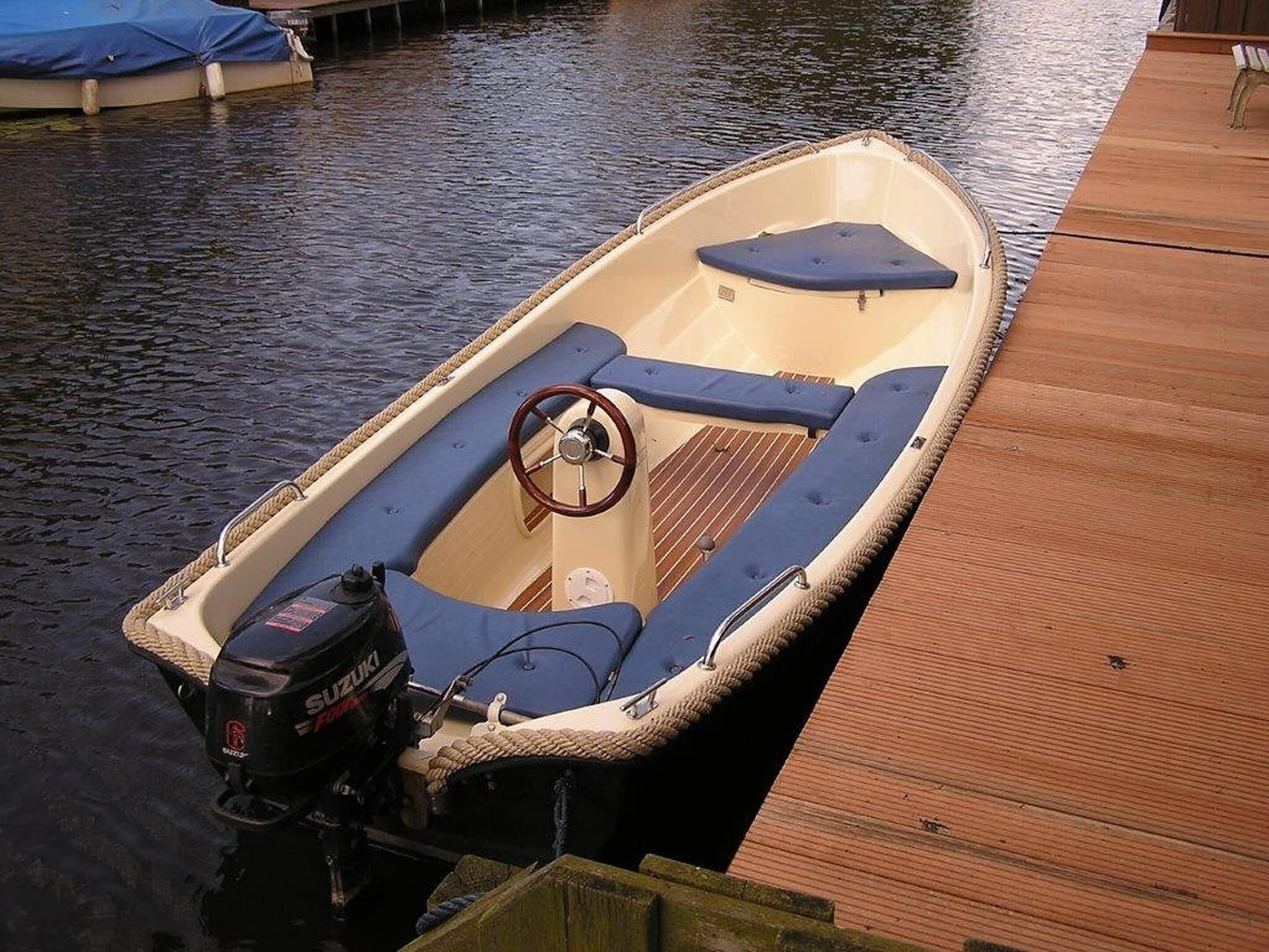 A small motorboat with a steering wheel, blue cushions, and a Suzuki outboard motor.