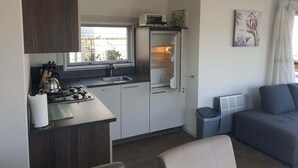 Une cuisine compacte équipée d’une cuisinière à gaz, d’un évier et d’un réfrigérateur. Une fenêtre se trouve au-dessus de l’évier et un petit radiateur est fixé au mur.