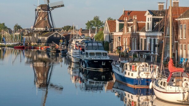 Un canal con barcos amarrados, un molino y edificios tradicionales.