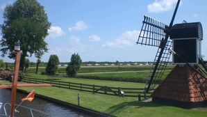 Un canal con barcos, un molino de viento y una zona verde con árboles.