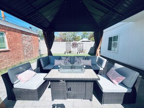 Une terrasse extérieure dotée d’un espace salon couvert, d’une table à plateau en verre et de meubles en osier.