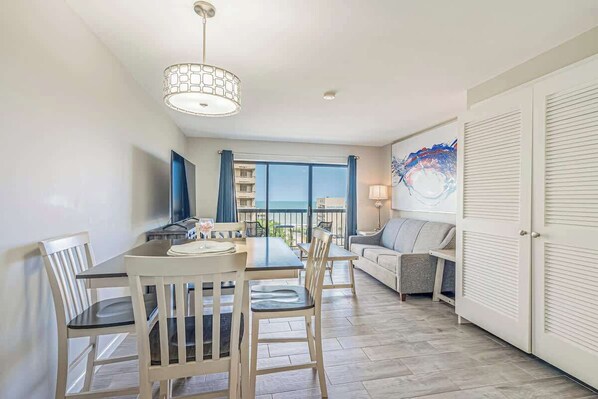 Habitación de hotel moderna con zona de comedor, sofá y un amplio ventanal con vistas al mar.