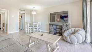 A modern living room with a dining area, a fireplace, and a large window with curtains. - 1BR - Sleeps 6 - Steps to The Beach - Pool - 7500 (Myrtle Beach)