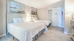 A hotel room with two beds, a painting on the wall, a lamp, and a door leading to another room. - 1BR - Sleeps 6 - Steps to The Beach - Pool - 7500 (Myrtle Beach)
