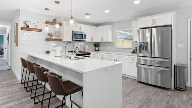 A modern kitchen with white cabinets, stainless steel appliances, and a central island with bar stools. - POSH LIVING in Fort Walton Beach (Fort Walton Beach)