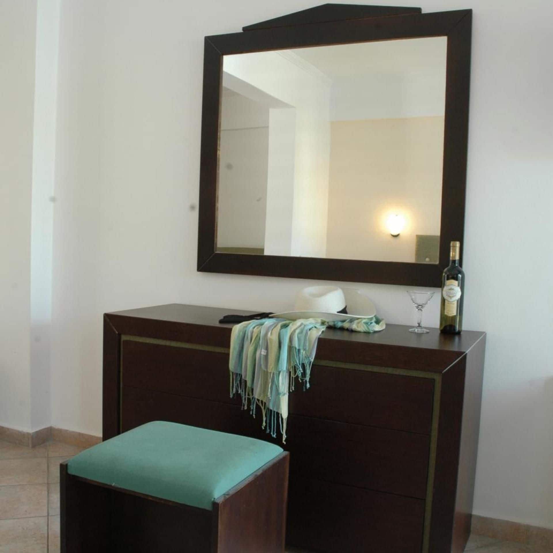 A room with a dark wooden dresser, a mirror above it, a bottle of wine, a glass, and a bench with a green cushion.